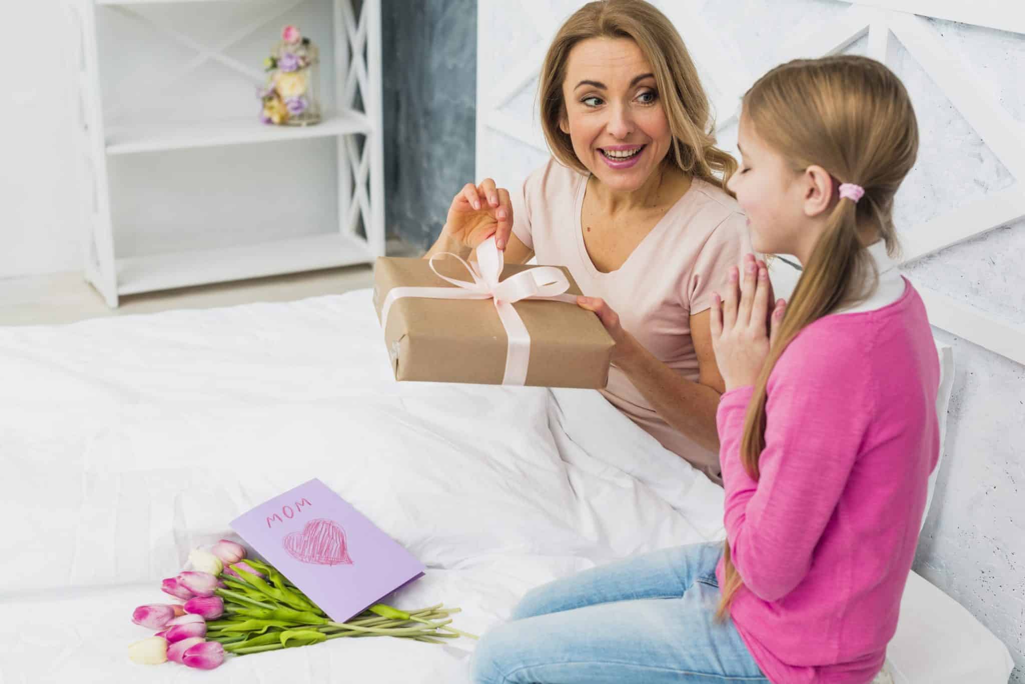 mother-daughter-sitting-bed-with-gift-scaled