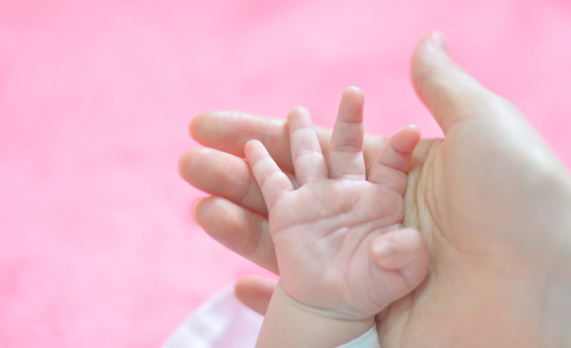 Main de bébé tenant le doigt d’un parent sur fond rose