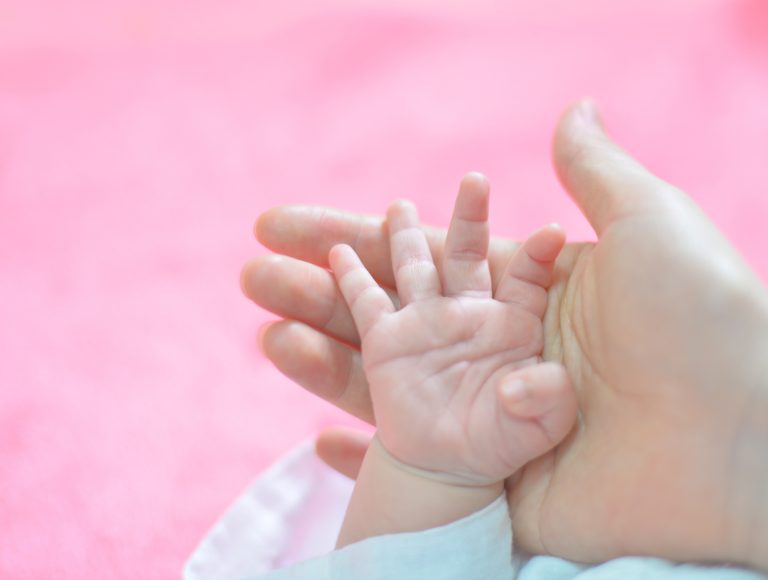 Main de bébé tenant le doigt d’un parent sur fond rose