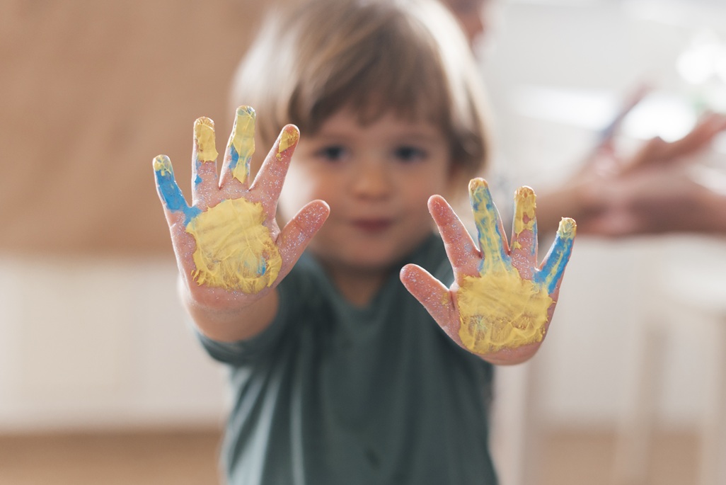 Enfant montrant ses mains recouvertes de peinture jaune et bleue après une activité créative à la maison