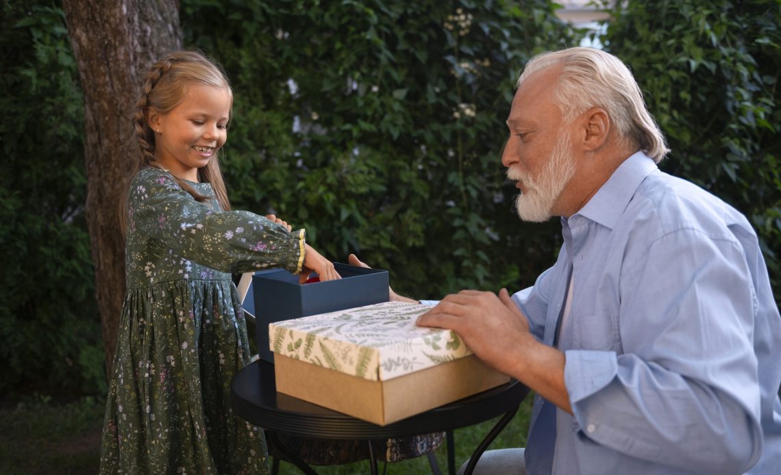 Petite fille offrant un cadeau à son grand-père dans le jardin lors d’un moment familial