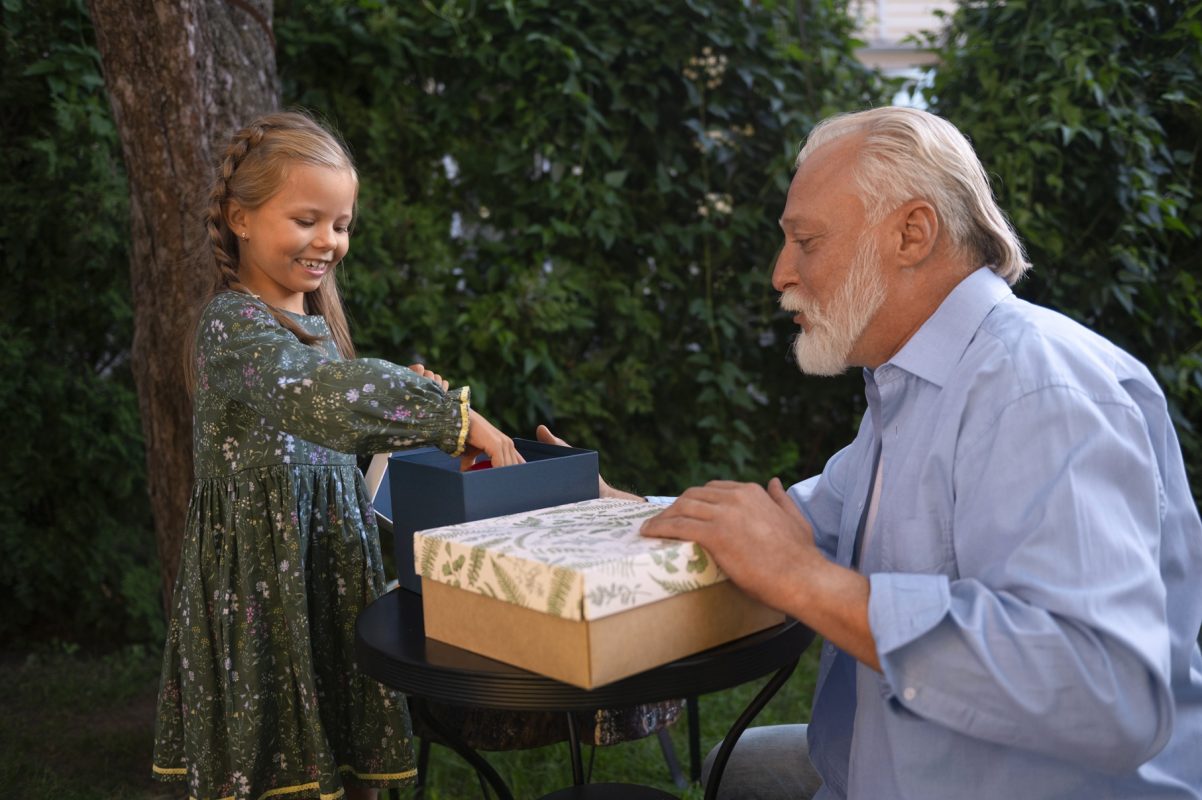 Petite fille offrant un cadeau à son grand-père dans le jardin lors d’un moment familial