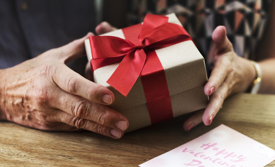 Mains d’un couple échangeant un cadeau emballé avec un ruban rouge pour la Saint-Valentin