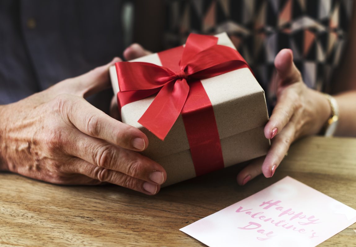 Mains d’un couple échangeant un cadeau emballé avec un ruban rouge pour la Saint-Valentin