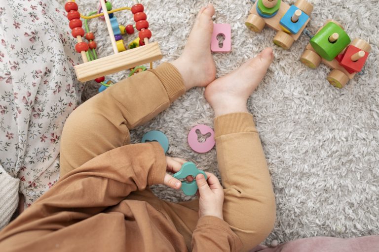 Pieds d’un bébé assis sur un tapis entouré de jouets en bois et d’une petite voiture