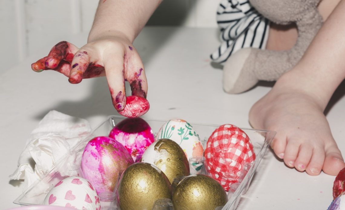 Bébé avec les mains pleines de peinture colorée décorant des œufs lors d’une activité créative