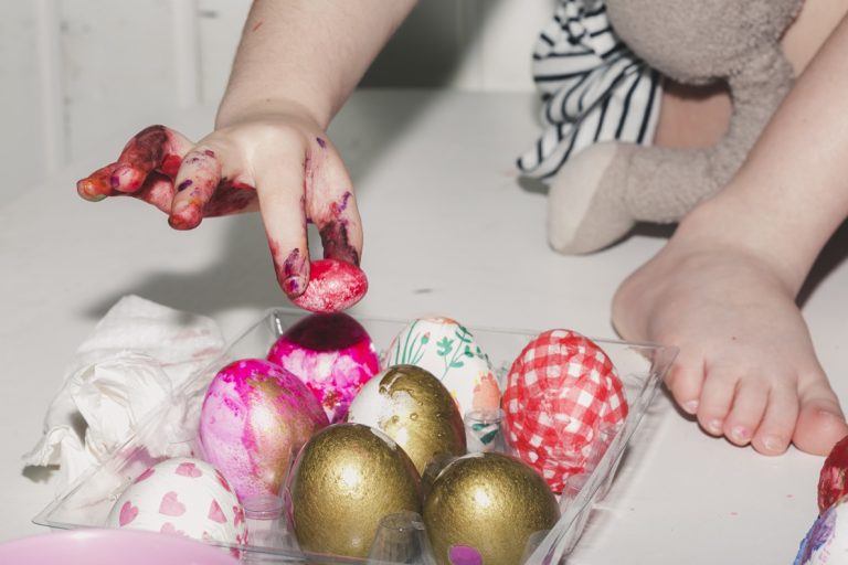 Bébé avec les mains pleines de peinture colorée décorant des œufs lors d’une activité créative